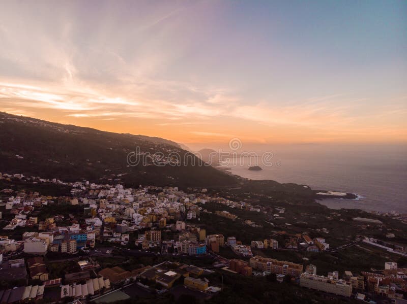 Ηλιοβασίλεμα Tenerife στο Βορρά με τον απότομο βράχο και έναν βράχο στη μέση της θάλασσας και μιας πόλης Εικόνα από τον κηφήνα στοκ φωτογραφία με δικαίωμα ελεύθερης χρήσης Ηλιοβασίλεμα Tenerife στο Βορρά με τον απότομο βράχο και έναν βράχο στη μέση της θάλασσας και μιας πόλης Εικόνα από τον κηφήνα στοκ φωτογραφία με δικαίωμα ελεύθερης χρήσης