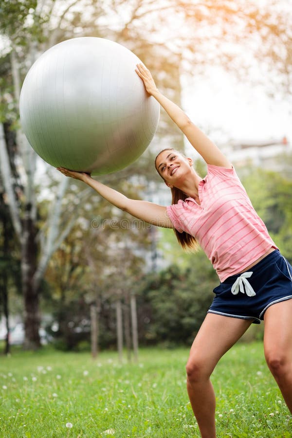 Νέα γυναίκα που ασκεί με τη σφαίρα pilates στο πάρκο Σφαίρα ικανότητας εκμετάλλευσης εκπαιδευτικών γιόγκας πέρα από το κεφάλι και στοκ εικόνες με δικαίωμα ελεύθερης χρήσης Νέα γυναίκα που ασκεί με τη σφαίρα pilates στο πάρκο Σφαίρα ικανότητας εκμετάλλευσης εκπαιδευτικών γιόγκας πέρα από το κεφάλι και στοκ εικόνες με δικαίωμα ελεύθερης χρήσης
