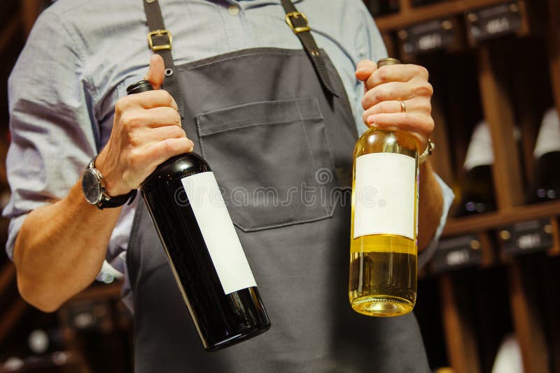 Νέο πιό sommelier μπουκάλι εκμετάλλευσης του κόκκινου κρασιού στο κελάρι στοκ φωτογραφία με δικαίωμα ελεύθερης χρήσης Νέο πιό sommelier μπουκάλι εκμετάλλευσης του κόκκινου κρασιού στο κελάρι στοκ φωτογραφία με δικαίωμα ελεύθερης χρήσης