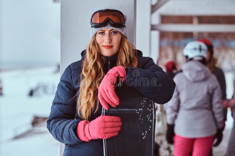 Ξανθή γυναίκα που φορά χειμερινό sportswear την τοποθέτηση με ένα σνόουμπορντ στοκ φωτογραφία με δικαίωμα ελεύθερης χρήσης Ξανθή γυναίκα που φορά χειμερινό sportswear την τοποθέτηση με ένα σνόουμπορντ στοκ φωτογραφία με δικαίωμα ελεύθερης χρήσης