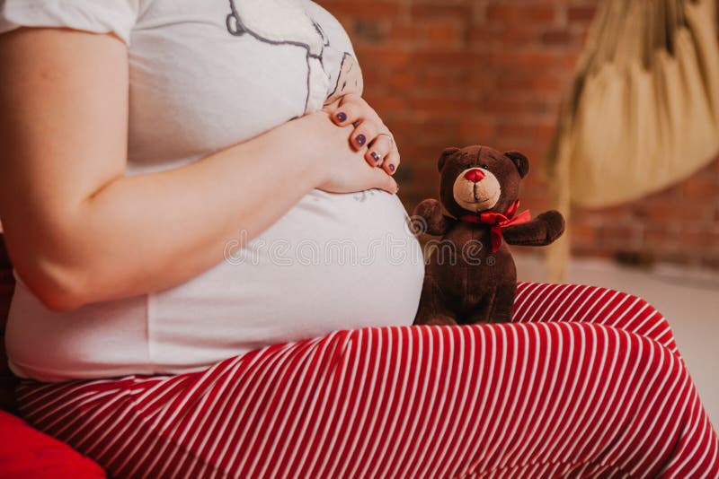 Έγκυος γυναίκα στις πυτζάμες που κρατά μια teddy αρκούδα στο κρεβάτι στην κρεβατοκάμαρα στοκ εικόνες Έγκυος γυναίκα στις πυτζάμες που κρατά μια teddy αρκούδα στο κρεβάτι στην κρεβατοκάμαρα στοκ εικόνες