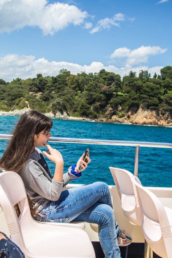 Ένα νέο κορίτσι με μακρυμάλλη εξετάζει το τηλέφωνο καθμένος σε ένα σκάφος αναψυχής. Το κορίτσι εφήβων απολαμβάνει τις διακοπές άνοιξη σε ένα ταξίδι θάλασσας σε ένα σκάφος αναψυχής Κάθεται στην ανώτερη γέφυρα επικοινωνεί από την τηλεοπτική κλήση