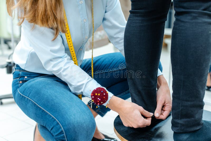 Ράφτης αλλαγών που μετρά το παντελόνι σε έναν πελάτη στοκ εικόνα