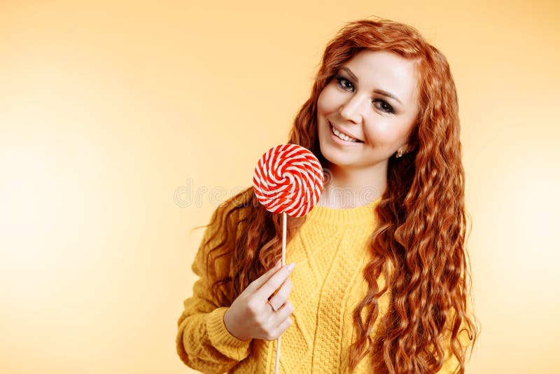 Όμορφη νέα σγουρή redhead γυναίκα που κρατά ένα κόκκινα άσπρα lollipop και ένα χαμόγελο στοκ φωτογραφία Όμορφη νέα σγουρή redhead γυναίκα που κρατά ένα κόκκινα άσπρα lollipop και ένα χαμόγελο στοκ φωτογραφία