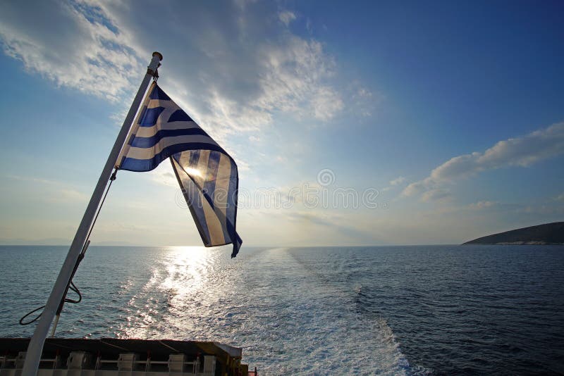 Όμορφο ηλιοβασίλεμα πέρα από τη θάλασσα με την ελληνική σημαία στο πρώτο πλάνο που αντιμετωπίζεται από το πορθμείο στη διαδρομή σ στοκ φωτογραφία με δικαίωμα ελεύθερης χρήσης Όμορφο ηλιοβασίλεμα πέρα από τη θάλασσα με την ελληνική σημαία στο πρώτο πλάνο που αντιμετωπίζεται από το πορθμείο στη διαδρομή σ στοκ φωτογραφία με δικαίωμα ελεύθερης χρήσης