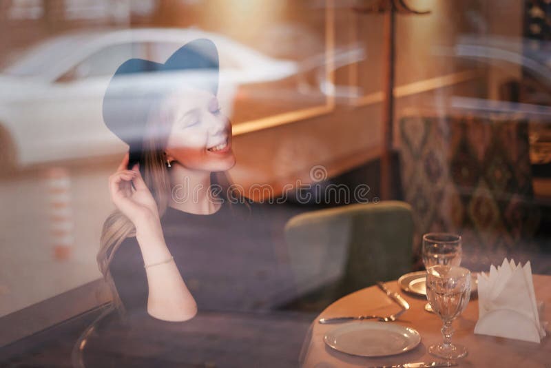 Όμορφο χαμόγελο νεολαιών και ευτυχής γυναίκα ξανθά στο καπέλο στον πίνακα εστιατορίων μέσω του γυαλιού Αντανακλάσεις στοκ φωτογραφία με δικαίωμα ελεύθερης χρήσης Όμορφο χαμόγελο νεολαιών και ευτυχής γυναίκα ξανθά στο καπέλο στον πίνακα εστιατορίων μέσω του γυαλιού Αντανακλάσεις στοκ φωτογραφία με δικαίωμα ελεύθερης χρήσης