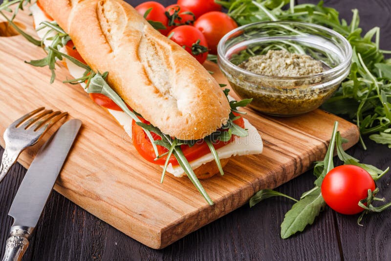 Ψημένο panini με το σάντουιτς ζαμπόν, τυριών και arugula στον τέμνοντα πίνακα στοκ εικόνες με δικαίωμα ελεύθερης χρήσης Ψημένο panini με το σάντουιτς ζαμπόν, τυριών και arugula στον τέμνοντα πίνακα στοκ εικόνες με δικαίωμα ελεύθερης χρήσης
