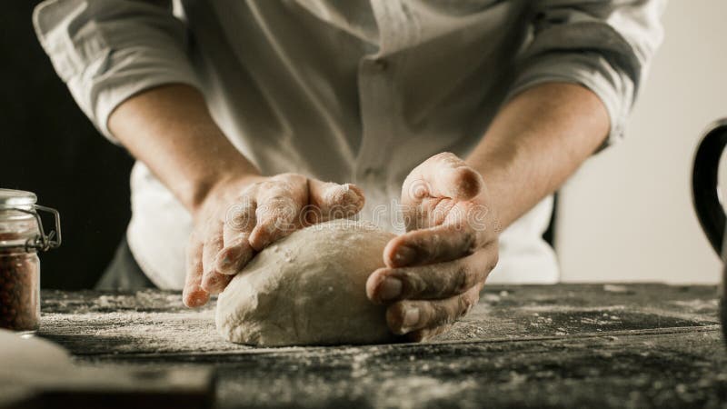 Τα αρσενικά χέρια αρχιμαγείρων ζυμώνουν τη ζύμη με το αλεύρι στον πίνακα κουζινών στοκ εικόνες Τα αρσενικά χέρια αρχιμαγείρων ζυμώνουν τη ζύμη με το αλεύρι στον πίνακα κουζινών στοκ εικόνες