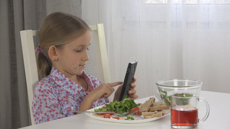 Ταμπλέτα παιχνιδιού παιδιών, χρήση Smartphone παιδιών που τρώει τα αυγά, μαρούλι σαλάτας στο πρόγευμα στοκ εικόνα με δικαίωμα ελεύθερης χρήσης