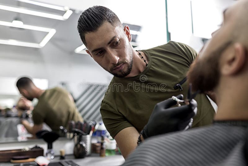 Το μοντέρνο άτομο με μια γενειάδα κάθεται μπροστά από τον καθρέφτη σε ένα barbershop Γενειάδα των ατόμων περιποιήσεων κουρέων με στοκ εικόνες με δικαίωμα ελεύθερης χρήσης Το μοντέρνο άτομο με μια γενειάδα κάθεται μπροστά από τον καθρέφτη σε ένα barbershop Γενειάδα των ατόμων περιποιήσεων κουρέων με στοκ εικόνες με δικαίωμα ελεύθερης χρήσης
