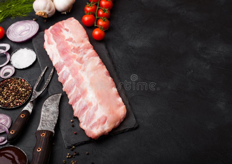 Φρέσκα ακατέργαστα πλευρά χοιρινού κρέατος στον τεμαχίζοντας πίνακα και το εκλεκτής ποιότητας δίκρανο κρέατος και μαχαίρι στο μαύ στοκ φωτογραφίες με δικαίωμα ελεύθερης χρήσης Φρέσκα ακατέργαστα πλευρά χοιρινού κρέατος στον τεμαχίζοντας πίνακα και το εκλεκτής ποιότητας δίκρανο κρέατος και μαχαίρι στο μαύ στοκ φωτογραφίες με δικαίωμα ελεύθερης χρήσης