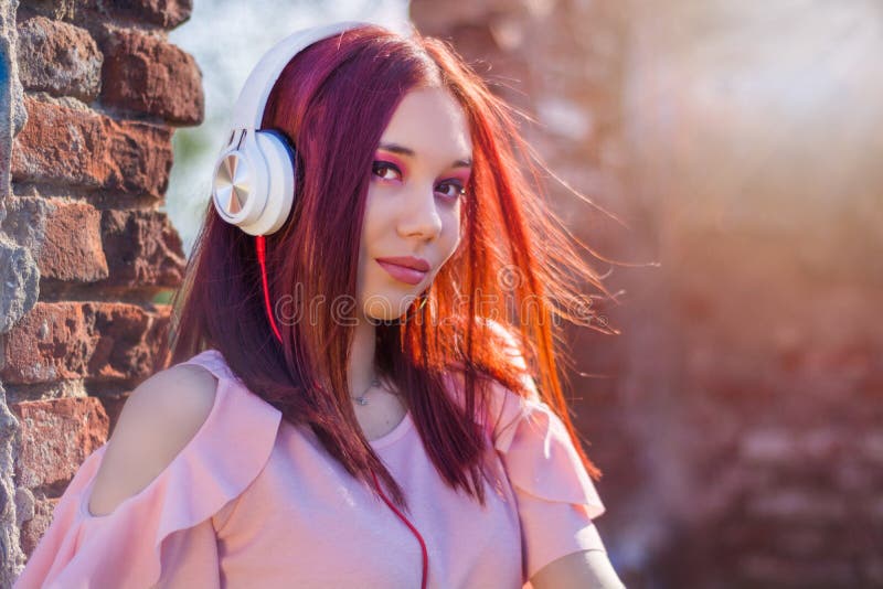 Πανέμορφη μουσική γυναικείου ακούσματος redheads στα ακουστικά στο θολωμένο υπόβαθρο και τα κόκκινα τούβλα τοίχων στο ηλιοβασίλεμ στοκ εικόνες Πανέμορφη μουσική γυναικείου ακούσματος redheads στα ακουστικά στο θολωμένο υπόβαθρο και τα κόκκινα τούβλα τοίχων στο ηλιοβασίλεμ στοκ εικόνες