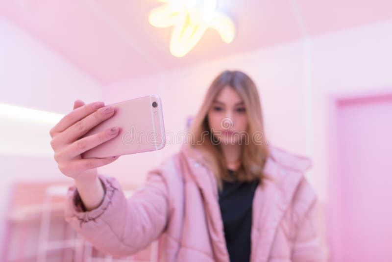 Девушка в розовых одеждах делает фото на розовом смартфоне в розовой комнате Розовая жизнь Фокус на вашем телефоне стоковое фото rf Девушка в розовых одеждах делает фото на розовом смартфоне в розовой комнате Розовая жизнь Фокус на вашем телефоне стоковое фото rf