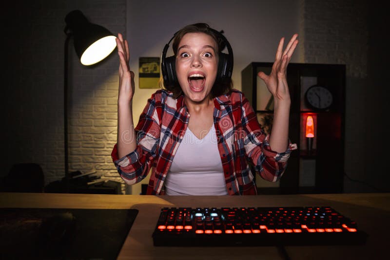Возбужденный gamer девушки сидя на таблице, играя Онлайн-игры стоковые фото Возбужденный gamer девушки сидя на таблице, играя Онлайн-игры стоковые фото