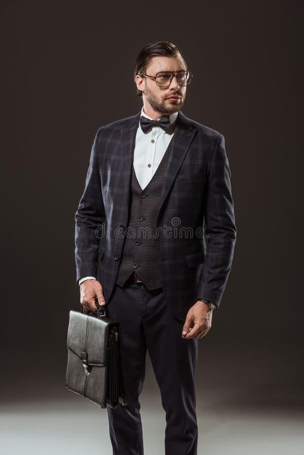 красивое buisnessman в eyeglasses костюма и портфеле удерживания бабочки и смотреть прочь стоковая фотография