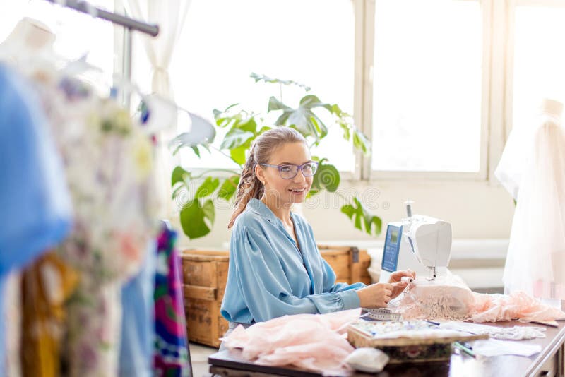 Молодой женский портной сидит на рабочем месте и выбирает цвет потоков в atelier стоковая фотография rf Молодой женский портной сидит на рабочем месте и выбирает цвет потоков в atelier стоковая фотография rf