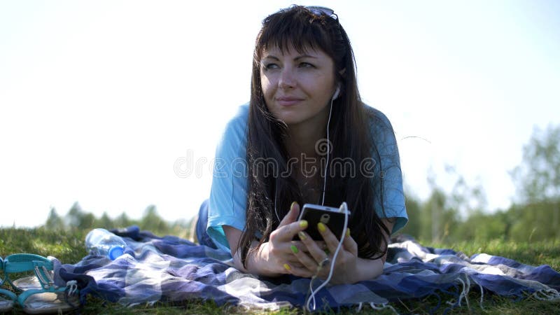 Молодая женщина ослабляя outdoors слушать музыку и усмехаться стоковое фото Молодая женщина ослабляя outdoors слушать музыку и усмехаться стоковое фото