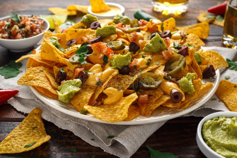 Мексиканские обломоки tortilla nachos с оливками, jalapeno, гуакамоле, томатами сальсой, пивом dipand сыра стоковые фотографии rf Мексиканские обломоки tortilla nachos с оливками, jalapeno, гуакамоле, томатами сальсой, пивом dipand сыра стоковые фотографии rf