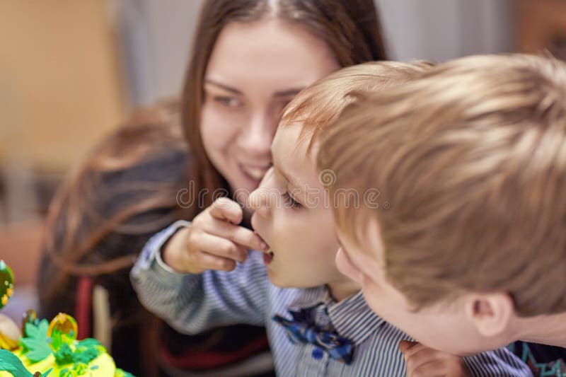 Милый кавказский белокурый мальчик ест sweeties от именниного пирога сидя между родителями стоковая фотография rf Милый кавказский белокурый мальчик ест sweeties от именниного пирога сидя между родителями стоковая фотография rf