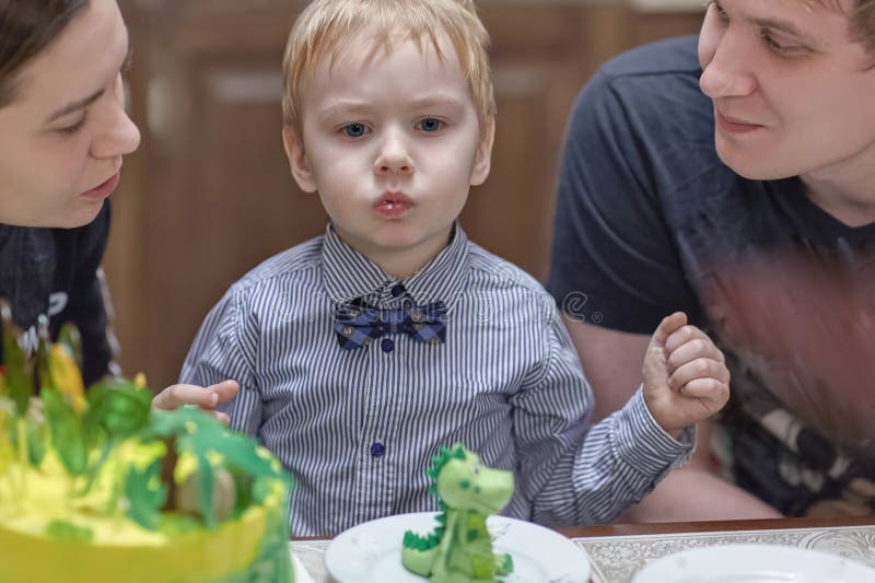 Милый кавказский белокурый мальчик ест sweeties от именниного пирога сидя между родителями стоковые изображения rf Милый кавказский белокурый мальчик ест sweeties от именниного пирога сидя между родителями стоковые изображения rf