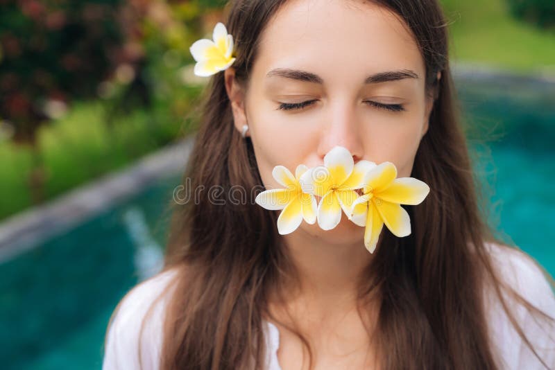 Портрет прекрасной девушки с закрытыми глазами и plumeria, цветков frangipani в ее предпосылке рта бассейна стоковое фото rf Портрет прекрасной девушки с закрытыми глазами и plumeria, цветков frangipani в ее предпосылке рта бассейна стоковое фото rf