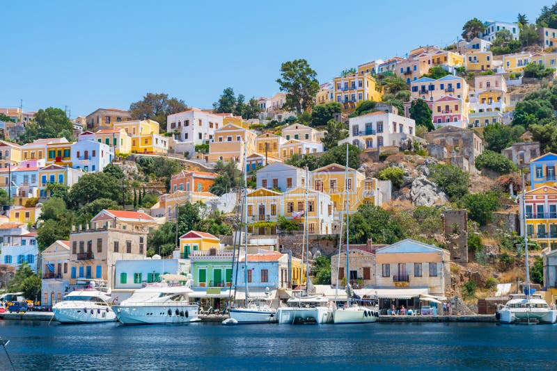Парусники, яхты и красочные дома в городке гавани острова Symi Symi, Греции стоковая фотография Парусники, яхты и красочные дома в городке гавани острова Symi Symi, Греции стоковая фотография