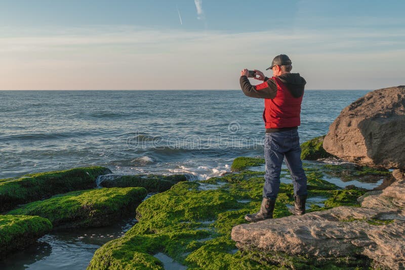 Путешественник на скалистом seashore перерастанном с зелеными водорослями фотографируя стоковая фотография rf Путешественник на скалистом seashore перерастанном с зелеными водорослями фотографируя стоковая фотография rf