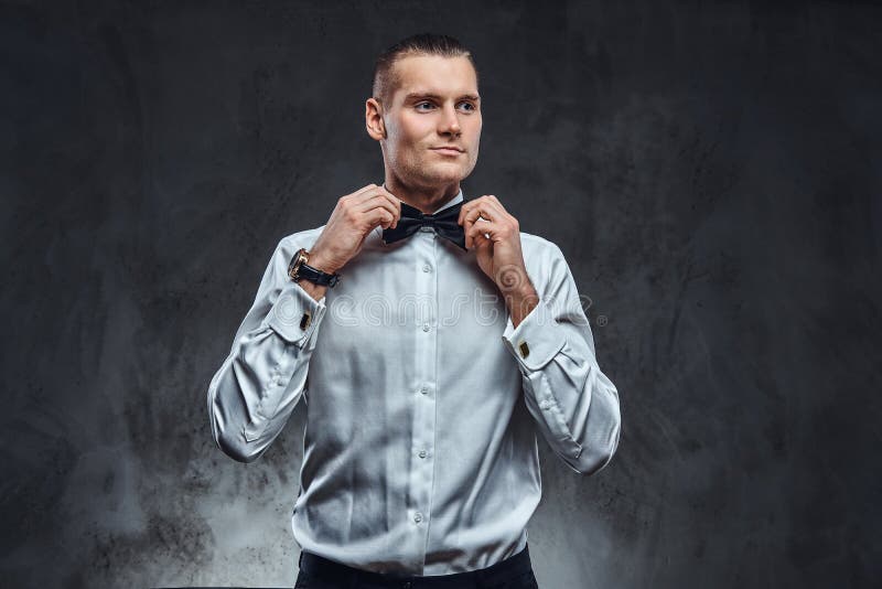 Элегантно одетая рубашка красивого человека нося белая исправляя его bowtie и смотря прочь стоковые фотографии rf Элегантно одетая рубашка красивого человека нося белая исправляя его bowtie и смотря прочь стоковые фотографии rf