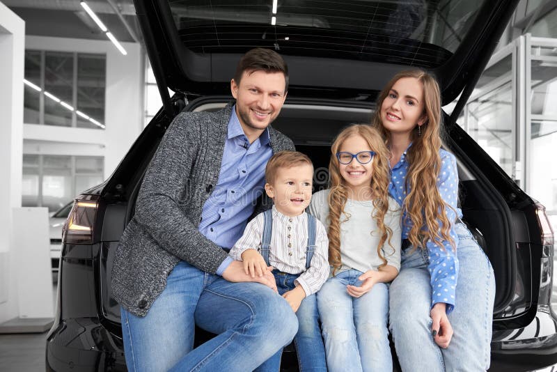 Счастливая семья сидя в космосе багажа автомобиля, представляя стоковые изображения Счастливая семья сидя в космосе багажа автомобиля, представляя стоковые изображения