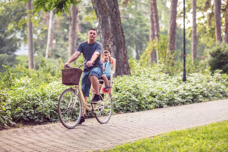 Счастливые велосипеды папы и сына ехать outdoors в парке города стоковая фотография Счастливые велосипеды папы и сына ехать outdoors в парке города стоковая фотография