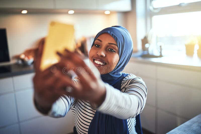 Усмехаясь молодая арабская женщина принимая selfies дома стоковая фотография