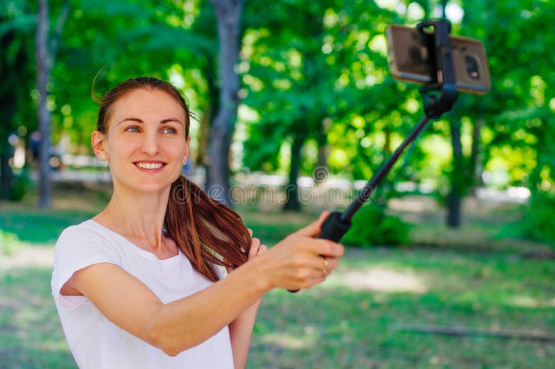 Усмехаясь молодая женщина принимая selfie по умному телефону используя st selfie стоковые фотографии rf Усмехаясь молодая женщина принимая selfie по умному телефону используя st selfie стоковые фотографии rf