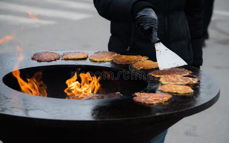 Человеческая рука варя золотые блинчики картошки на ярмарке города outdoors стоковые фотографии rf Человеческая рука варя золотые блинчики картошки на ярмарке города outdoors стоковые фотографии rf