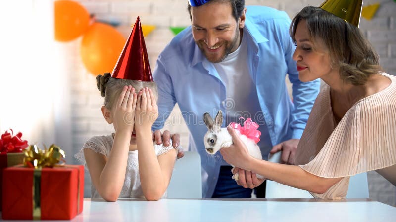 Родители представляя милый зайчика для дочери, девушки с глазами закрыли, b-дневная партия стоковая фотография Родители представляя милый зайчика для дочери, девушки с глазами закрыли, b-дневная партия стоковая фотография