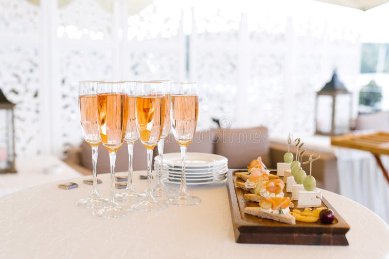 Óculos de champanhe cor-de-rosa na mesa do buffet ao lado de uma placa de aperitivos