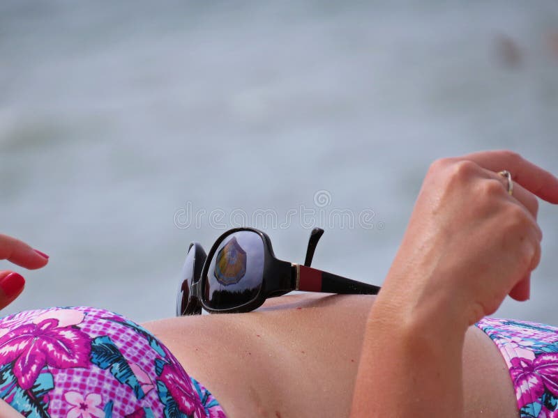 Óculos de sol que colocam na barriga da mulher na praia da areia com reflexão do guarda-chuva imagens de stock Óculos de sol que colocam na barriga da mulher na praia da areia com reflexão do guarda-chuva imagens de stock