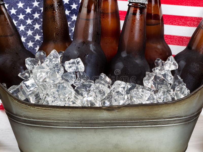 Close up of cold beer and ice in steel tub with American flag in background. Fourth of July holiday concept. Close up of cold beer and ice in steel tub with American flag in background. Fourth of July holiday concept.