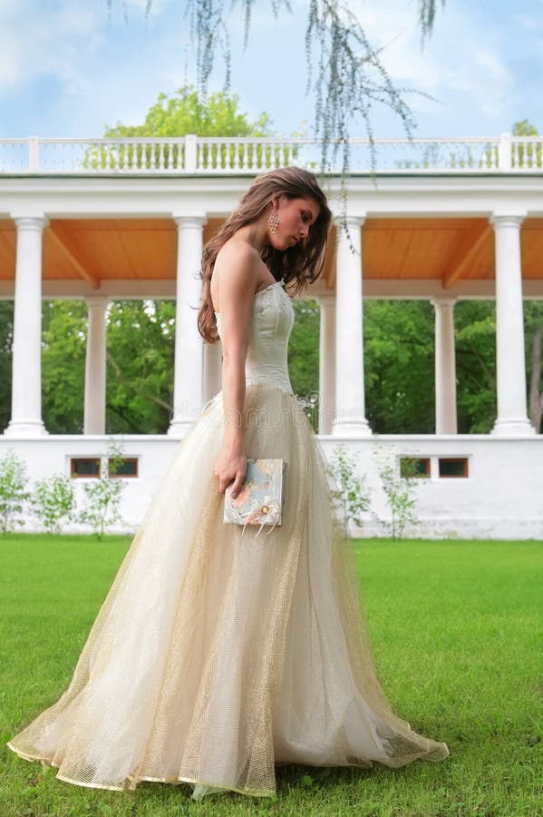 Beautiful princess with book walks on herb of the park near colonnades. Beautiful princess with book walks on herb of the park near colonnades