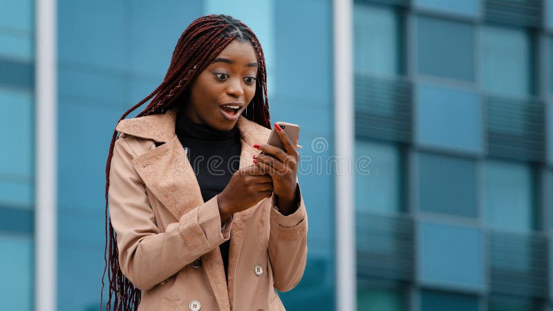 överraskad afrikansk amerikan-vinnare utomhus som läser goda nyheter om telefonfirande seger royaltyfri bild