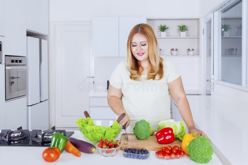 Överviktig kvinna som bereder grönsaker för att göra sallad fotografering för bildbyråer