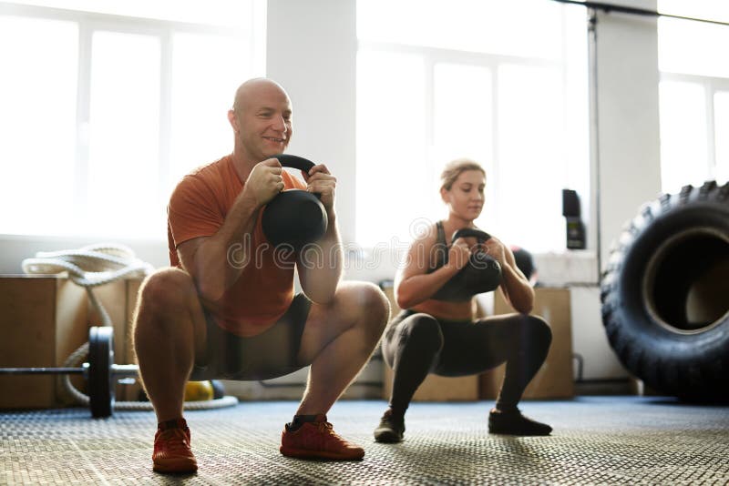 Strong men and women squatting while exercising with kettle bells. Strong men and women squatting while exercising with kettle bells