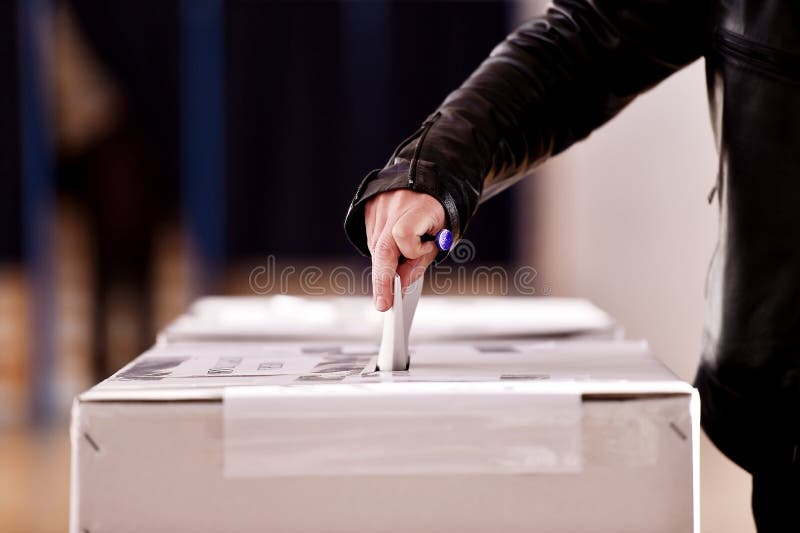 Hand of a person casting a vote into the ballot box during elections. Hand of a person casting a vote into the ballot box during elections