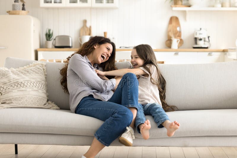 Überglücklich lachende junge Mutter kleine Tochter kitzelt auf Couch lizenzfreie stockfotografie
