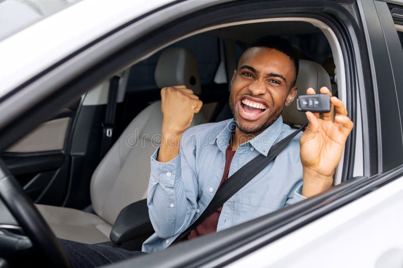 Überglücklicher schwarzer Typ, der Autoschlüssel hält und JA gestikuliert hat, der in einem neuen Auto sitzt und den Kauf moderner lizenzfreie stockbilder
