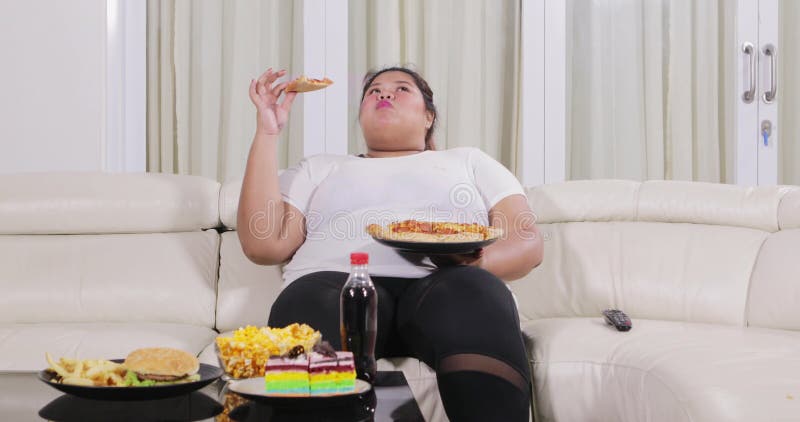 Überladene Frau, die Pizza auf Sofa isst