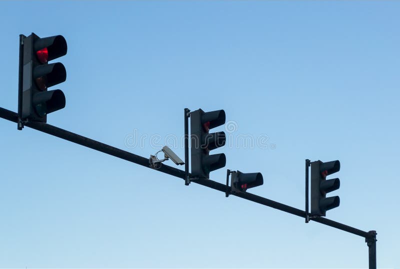 Überwachungskamera im Freien und vier rote Ampeln installiert auf einen Pfosten über einer Fahrbahn, gegen einen blauen Himmel, K