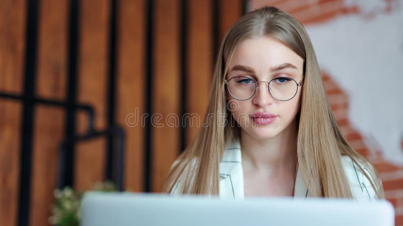 Überzeugte junge schöne Geschäftsfrau in den Gläsern denkend während des Arbeitens an Laptop-PC