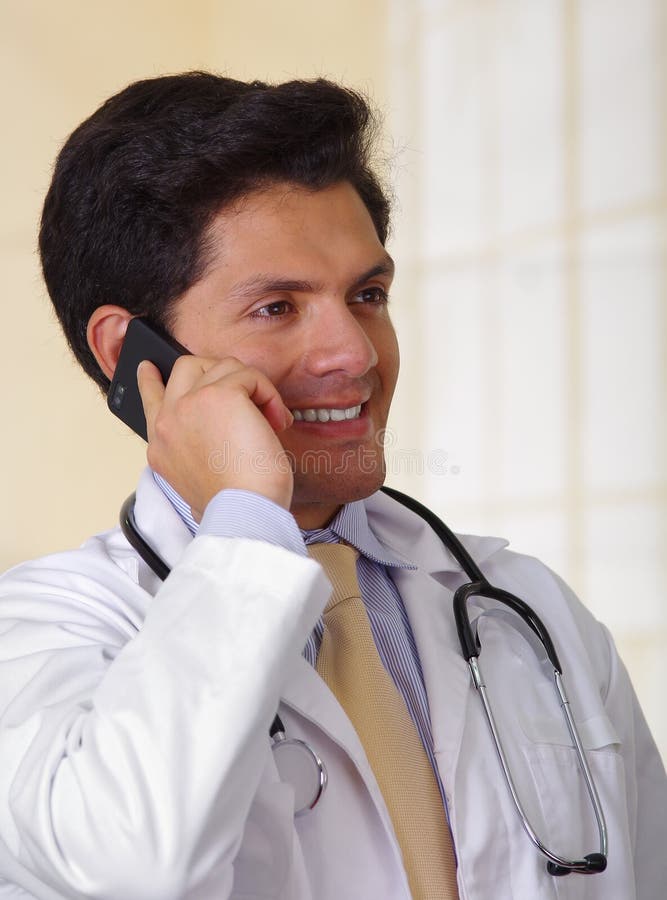 Überzeugter hübscher Doktor mit einem Stethoskop um seinen Hals, unter Verwendung eines celphone mit einer Hand, im Bürohintergru stockfotografie Überzeugter hübscher Doktor mit einem Stethoskop um seinen Hals, unter Verwendung eines celphone mit einer Hand, im Bürohintergru stockfotografie