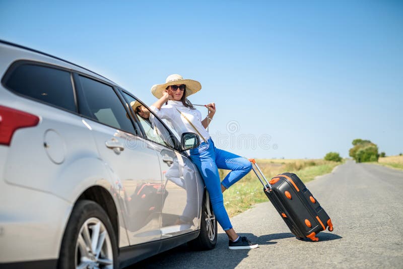 ładna dziewczyna z walizką stojącą w pobliżu samochodu i wiat na jej marzenie podróży