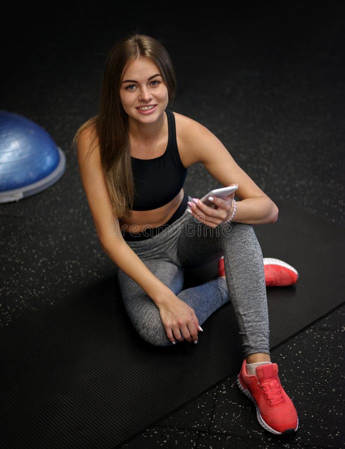 Ładna kobieta jest ubranym sporty munduruje z telefonem na gym tle Sprawność fizyczna, aktywność i bodybuilding pojęcie zdjęcie stock